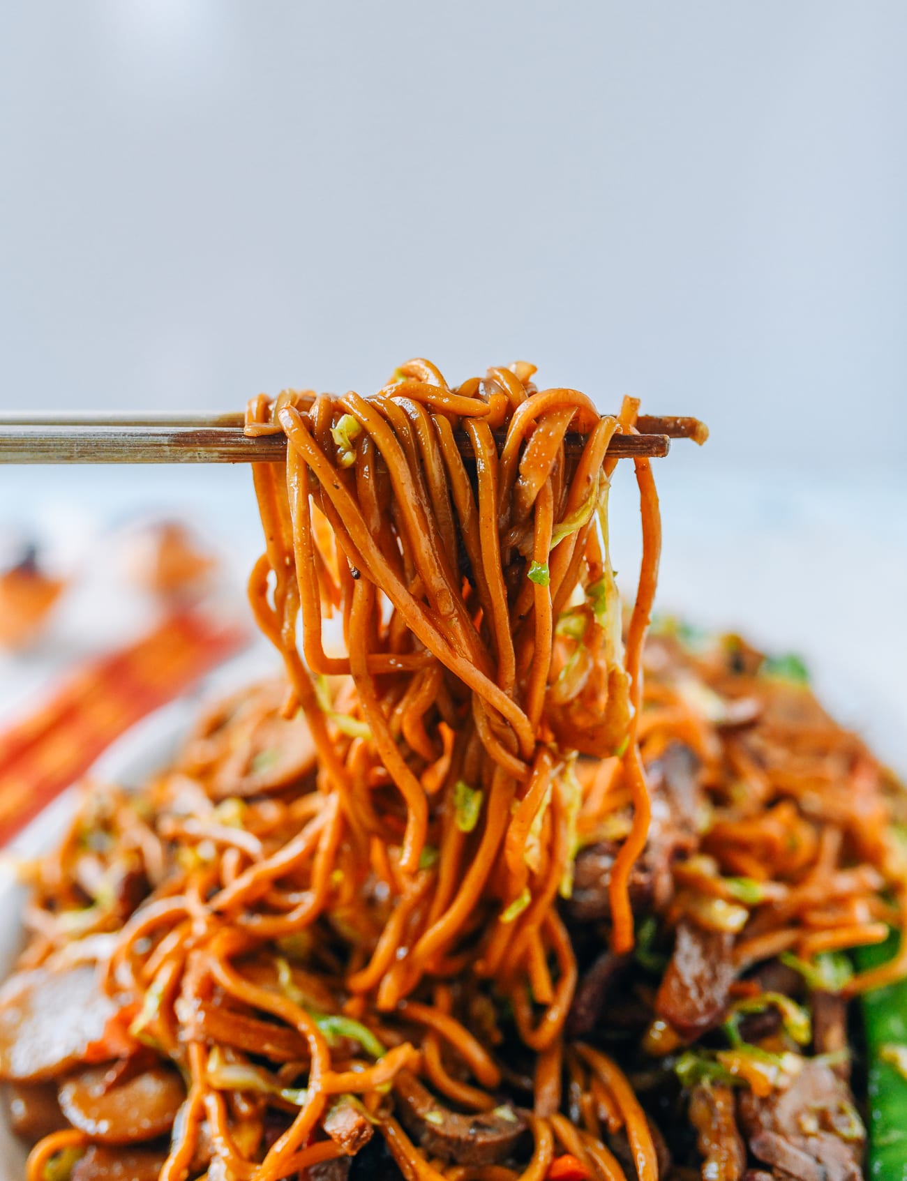 Pulling up strands of lo mein noodles with chopsticks